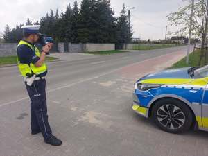 Umundurowany policjant trzyma w rękach urządzenie do pomiaru prędkości.