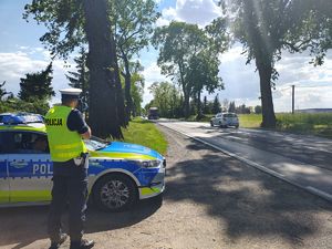 Na poboczu drogi umundurowany policjant mierzy prędkość nadjeżdżających pojazdów.