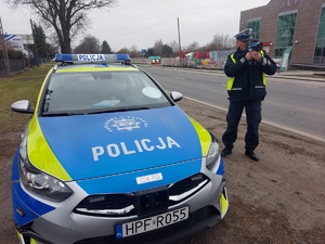 Na poboczu drogi umundurowany policjant mierzy prędkość nadjeżdżających pojazdów.
