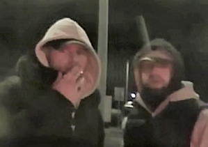Na parkingu w porze nocnej stoją dwaj mężczyźni, którzy mają zarost na twarzy i założone kaptury na głowę.