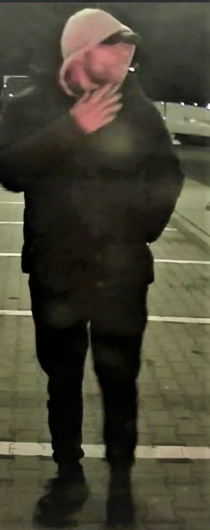 Na parkingu w porze nocnej stoją dwaj mężczyźni, którzy mają zarost na twarzy i założone kaptury na głowę.