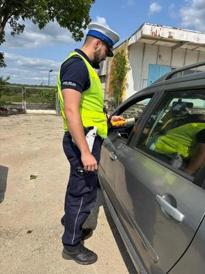 Umundurowany policjant alkomatem bada stan trzeźwości kierowcy samochodu.