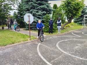 Policjanci przeprowadzają egzamin uczniów na kartę rowerowa na miasteczku ruchu drogowego przy szkole.