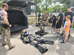 Piknik przed budynkiem komendy, rozstawione są namioty wystawców, pojazdy służb mundurowych, osoby odwiedzają stoiska.