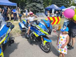 Piknik przed budynkiem komendy, rozstawione są namioty wystawców, pojazdy służb mundurowych, osoby odwiedzają stoiska.