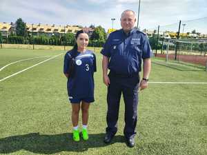 Na boisku policjantka z drużyny piłkarskiej w stroju sportowym  z Komendantem.