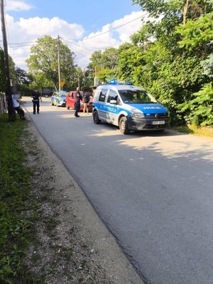 Na poboczu drogi stoją dwa policyjne radiowozy między nimi czerwony osobowy samochód, policjanci rozmawiają z kilkoma osobami.