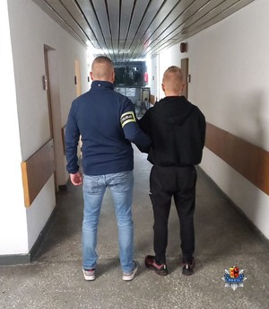 Na korytarzu komendy policjant prowadzi zatrzymanego.