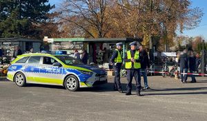 Na zdjęciu widać stojący radiowóz policyjny przed którym stoi dwóch umundurowanych policjantów.