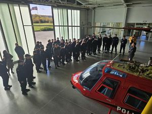 Na zdjęciu widać stojącą w pomieszczeniu hali młodzież wraz z opiekunami oraz policjantami. Tuż po przeciwnej stronie znajduje się czerwony helikopter.