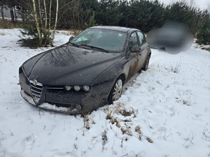 W komplecie leśnym stoi porzucony samochód koloru czarnego.