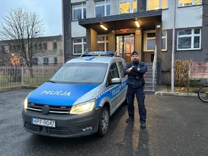 Na zdjęciu widać stojącego na tle budynku funkcjonariusza policji, który stoi przy radiowozie.
