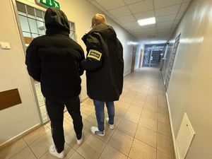 Na korytarzu policyjnego aresztu policjant prowadzi zatrzymanego mężczyznę.