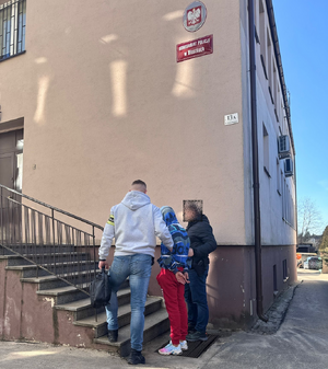 Na schodach komisariatu nieumundurowani policjanci prowadzą zatrzymanego mężczyznę.