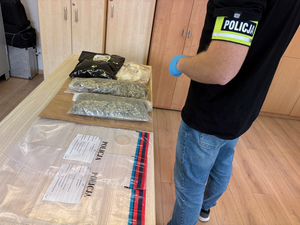 Na biurku leża torby foliowe z  narkotyki, obok stoi technik kryminalistyki.