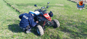 Na trawie stoi kład nad nim pochyla się umundurowany policjant.