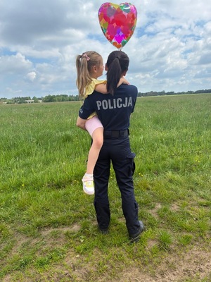 Umundurowana policjantka przytula dziewczynkę, która trzyma balonik.