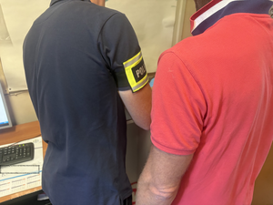 Technik kryminalistyki wykonuje daktyloskopię zatrzymanemu mężczyźnie.