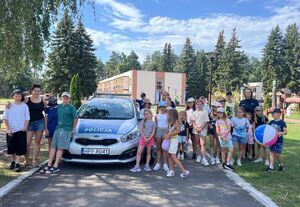 Na zdjęciu widać stojące obok radiowozu policyjnego dzieci wraz z policjantkami.