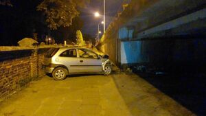 Betonowy parkan cmentarza obok stoi samochód, który uderzył w betonową podporę  wiaduktu.